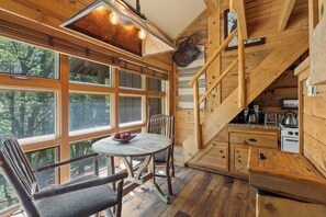 A rustic cabin interior with a dining area, wooden staircase, and a kitchen.