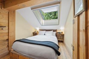 Une chambre avec une lucarne, des murs en bois, un lit, des tables de chevet et une petite table de nuit.