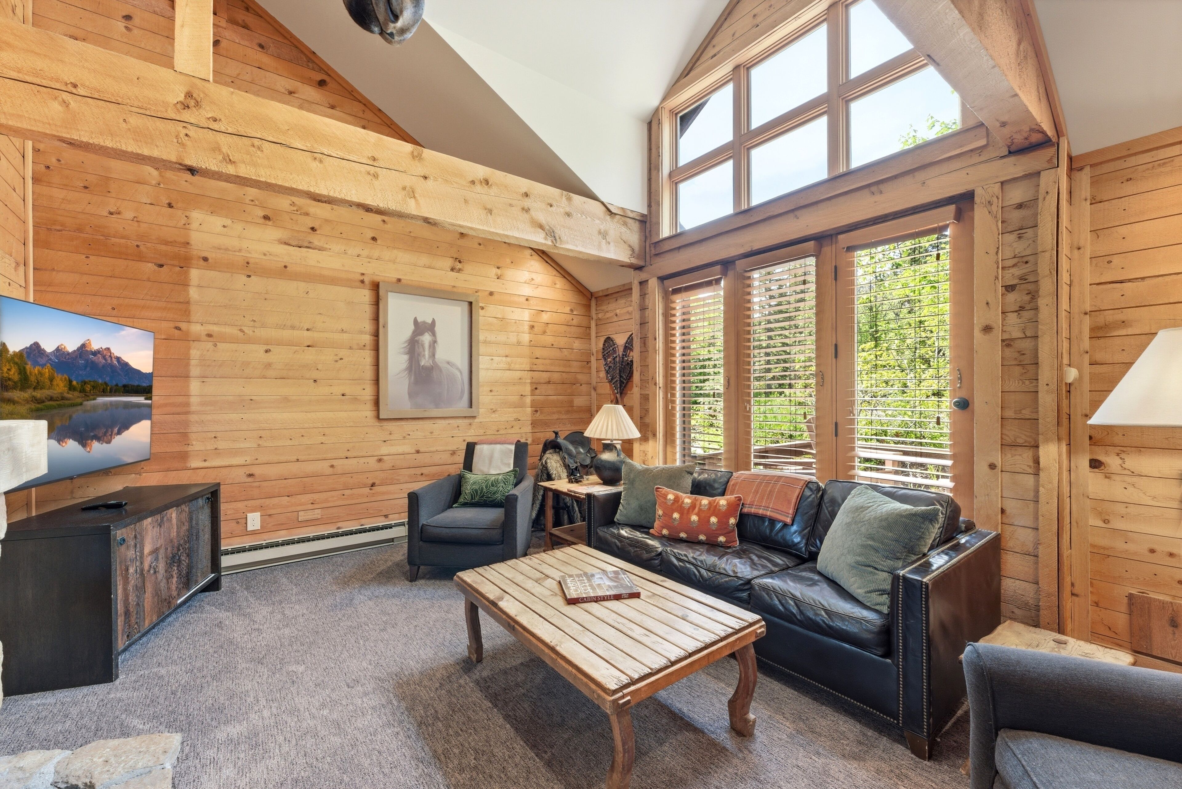 Un interior de madera con sofá, sillón, mesa de centro, televisor y chimenea.