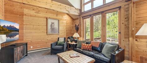 Un interior de madera con sofá, sillón, mesa de centro, televisor y chimenea.