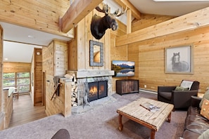 A log cabin interior with a fireplace, mounted animal head, framed picture, and a television.