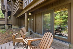 A wooden deck with two Adirondack chairs, a sliding glass door, and a view of a forested area. - Mandan Lower - King, Wood Burning Fireplace, Lower Level Sundance Cottage (Sundance)