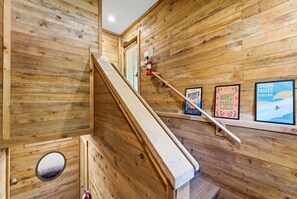 A wooden staircase with a fire extinguisher mounted on the wall, a small circular window, and framed posters on the wall. - Mandan Lower - King, Wood Burning Fireplace, Lower Level Sundance Cottage (Sundance)