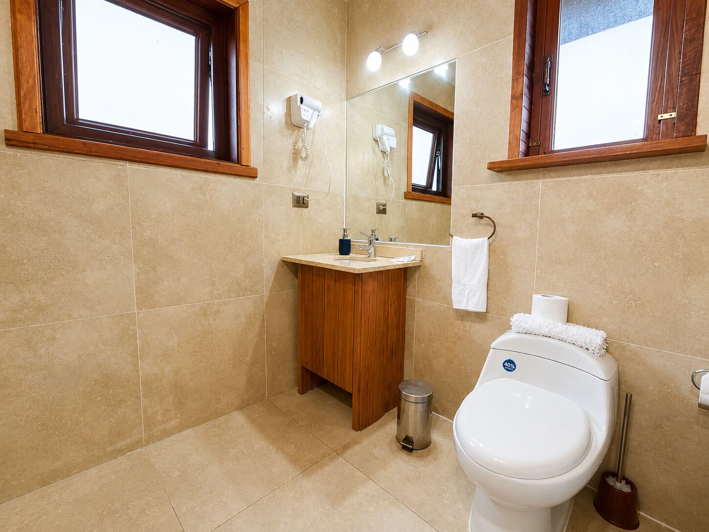 Un baño con tocador de madera, inodoro, espejo y ventana.