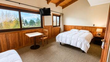 Une chambre à coucher comprenant un lit, un bureau, une chaise, un téléviseur et une fenêtre donnant sur des arbres.