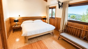 Un dormitorio con una cama de madera, lámparas de noche, una ventana con cortinas y vistas a zonas verdes.