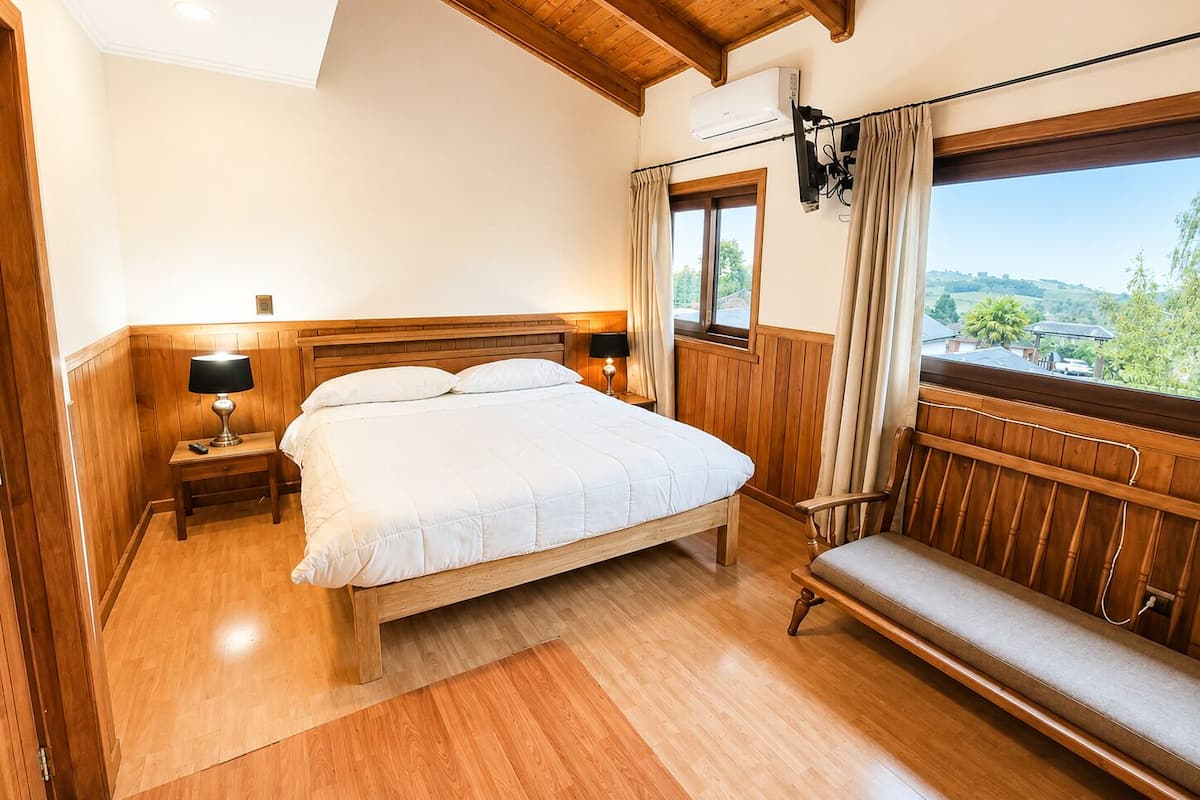 Un dormitorio con una cama de madera, lámparas de noche, una ventana con cortinas y vistas a zonas verdes.