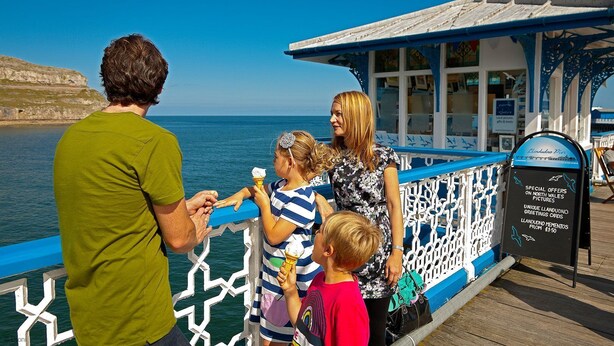 Un muelle con barandilla azul, un cartel y vista al mar.