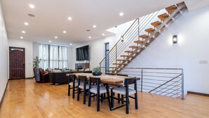 Uma sala ampla com uma mesa de jantar de madeira, cadeiras, um sofá e uma escada com degraus de madeira.