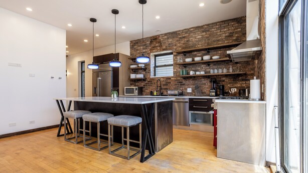 Cozinha moderna com ilha central, banquetas de bar e parede decorada com tijolos.