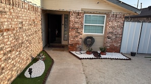 A house with a brick exterior, a welcome sign, a window, and a garden with plants and gravel. - Cozy home: A comfortable 2-bedroom house with a patio, barbecue, and exercise area (Odessa)