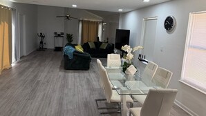 Ein modernes Wohnzimmer mit einem Glastisch, einer Couch, einem Deckenventilator und einem Fernseher.