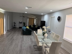 A modern living room with a glass dining table, a sofa, a ceiling fan, and a TV. - Cozy home: A comfortable 2-bedroom house with a patio, barbecue, and exercise area (Odessa)