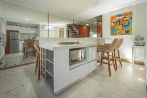 Een moderne keuken met een centraal eiland, inbouwapparatuur en een zithoek met barkrukken.