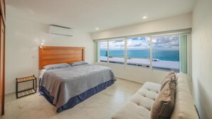 A bedroom with a bed, a window with a view of the sea, a wooden headboard, and a small table. - Elegant Stay Near the Beach 3403 (Cancún)
