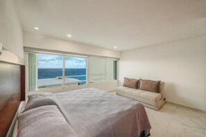 Une chambre d’hôtel avec un lit, un canapé, une grande fenêtre donnant sur la mer et un balcon.