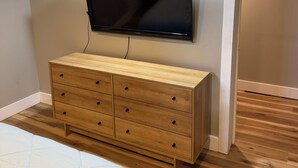 A bedroom with a bed, a wooden dresser, a flat-screen TV mounted on the wall, and a wooden floor. - Charming recently renovated house with AC, WiFi, in The Ashtabula Harbor (Ashtabula)