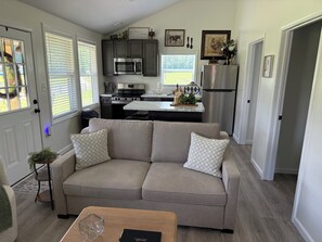 A modern kitchen with built-in appliances, a grey sofa with patterned cushions, and a wooden coffee table.