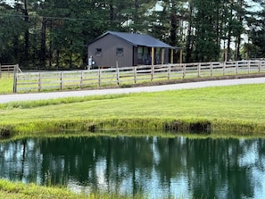 Un paysage rural avec une clôture en bois, un petit bâtiment et un étang.