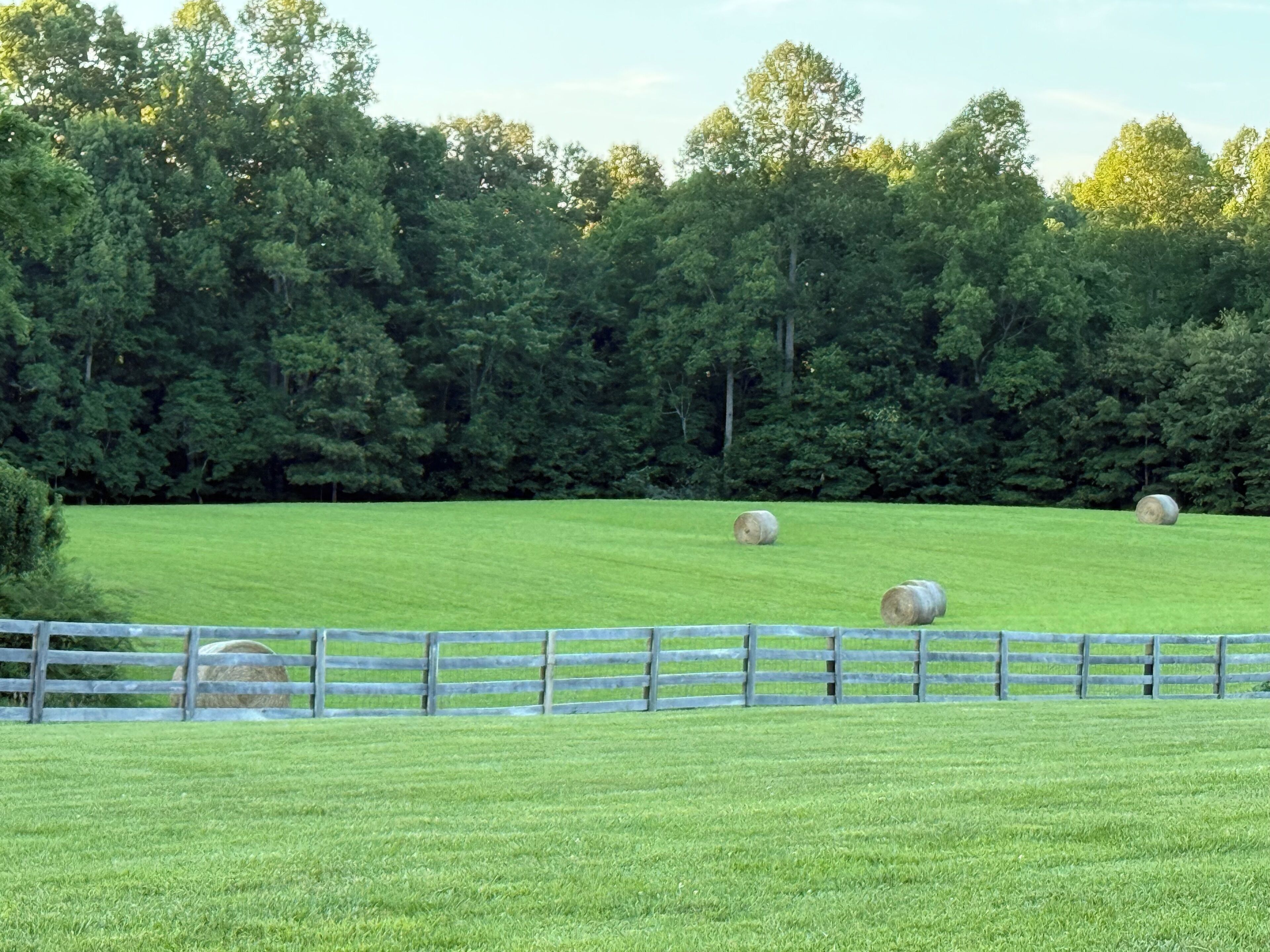 A grassy field with hay bales and a wooden fence.