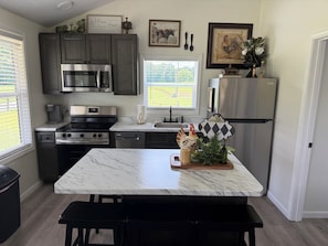 A kitchen with dark cabinets, stainless steel appliances, a marble countertop, and a view of the outdoors.