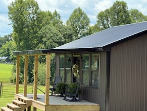 Een houten terras met een trap naar een overdekte veranda, een gebouw met grote ramen en een metalen dak.