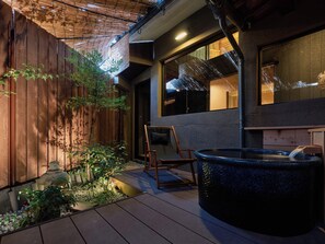 A wooden deck with a hot tub, a wooden fence, and a window overlooking a building.
