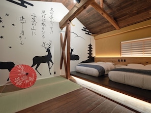 A room with a bed, wooden beams, a wall with deer and Japanese characters, and a red umbrella.