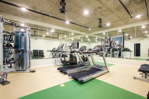 Ein Fitnessstudio mit Laufbändern, Kraftgeräten und einer Spiegelwand.