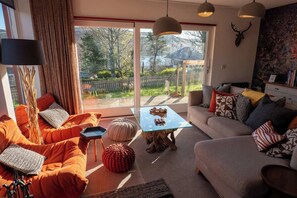 A living room with a sofa, coffee table, and a view of a garden through large windows.