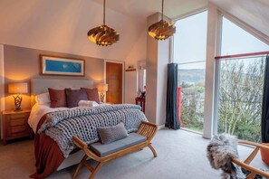 A bedroom with a large bed, bedside lamps, a window with a view, and a wooden bench.
