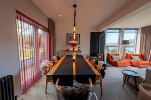 A modern living room with a long dining table, a fireplace, and a sofa with orange cushions.