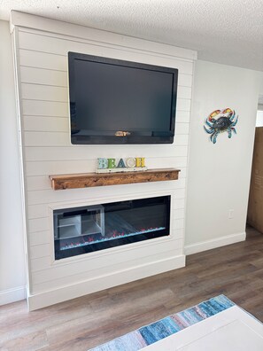 Ein Wohnzimmer mit Flachbildfernseher über einem Kamin, darunter ein Holzregal und eine dekorative Krabbe an der Wand.