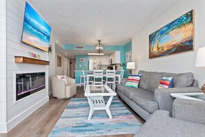 A living room with a fireplace, a sofa, a coffee table, and a TV mounted on the wall. - Amazing OceanView•14th-Fl• Spacious 3BR •Fireplace •Pool• Sleeps 10 (Myrtle Beach)
