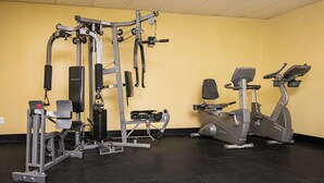 Een sportschool met diverse fitnessapparaten, waaronder een rek voor squats, een bankdrukapparaat en een elliptische machine.