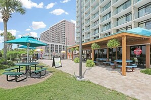 A hotel courtyard with outdoor seating, a signboard, and a building with multiple balconies. - Amazing OceanView•14th-Fl• Spacious 3BR •Fireplace •Pool• Sleeps 10 (Myrtle Beach)