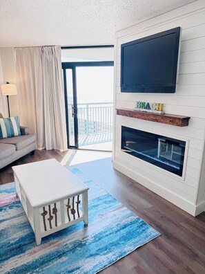 Ein Wohnzimmer mit einem wei ßen Sofa, einem weißen Couchtisch, einem Flachbildfernseher über einem Kamin und einem Balkon mit Geländer.