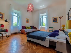 Ein Schlafzimmer mit einem Bett, einem Sessel, einer Stehlampe, einer Tischlampe und zwei Fenstern.