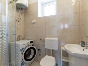 Ein Badezimmer mit Waschmaschine, Toilette, Waschbecken und einem Fenster.