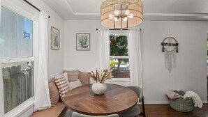 A dining area with a round wooden table, cushioned seating, a hanging light fixture, and a window with curtains. - Charming retreat with AC and outdoor oasis, just 3 blocks from Lafayette Hotel (San Diego)