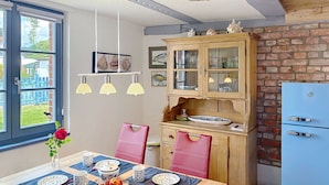 Comedor con mesa de madera dispuesta para cuatro personas, un refrigerador azul y una pared de ladrillo.