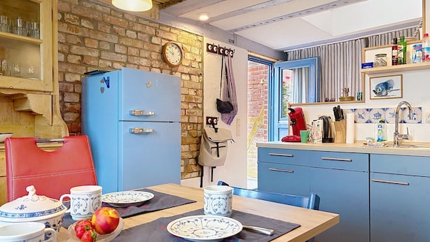 Una cocina con un refrigerador azul, armarios de madera y una mesa de comedor dispuesta con platos y un frutero.