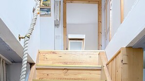 Una escalera de madera con barandal de cuerda que lleva a una puerta con un pequeño ventanal.
