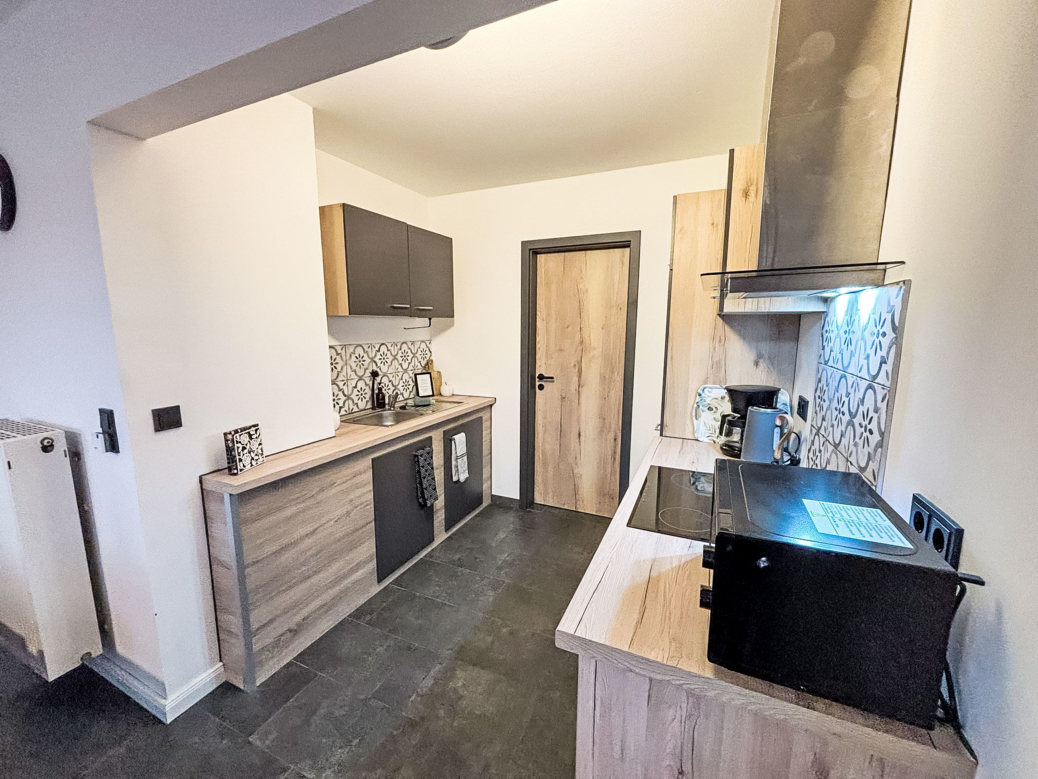 Eine moderne Küche mit Einbauherd, Mikrowelle und Spüle. Ein Holzschrank und eine Tür zu einem anderen Raum sind ebenfalls vorhanden.