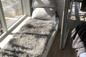 Ein Fensterplatz mit einem flauschigen Teppich, Kissen und Blick auf eine Holzterrasse.