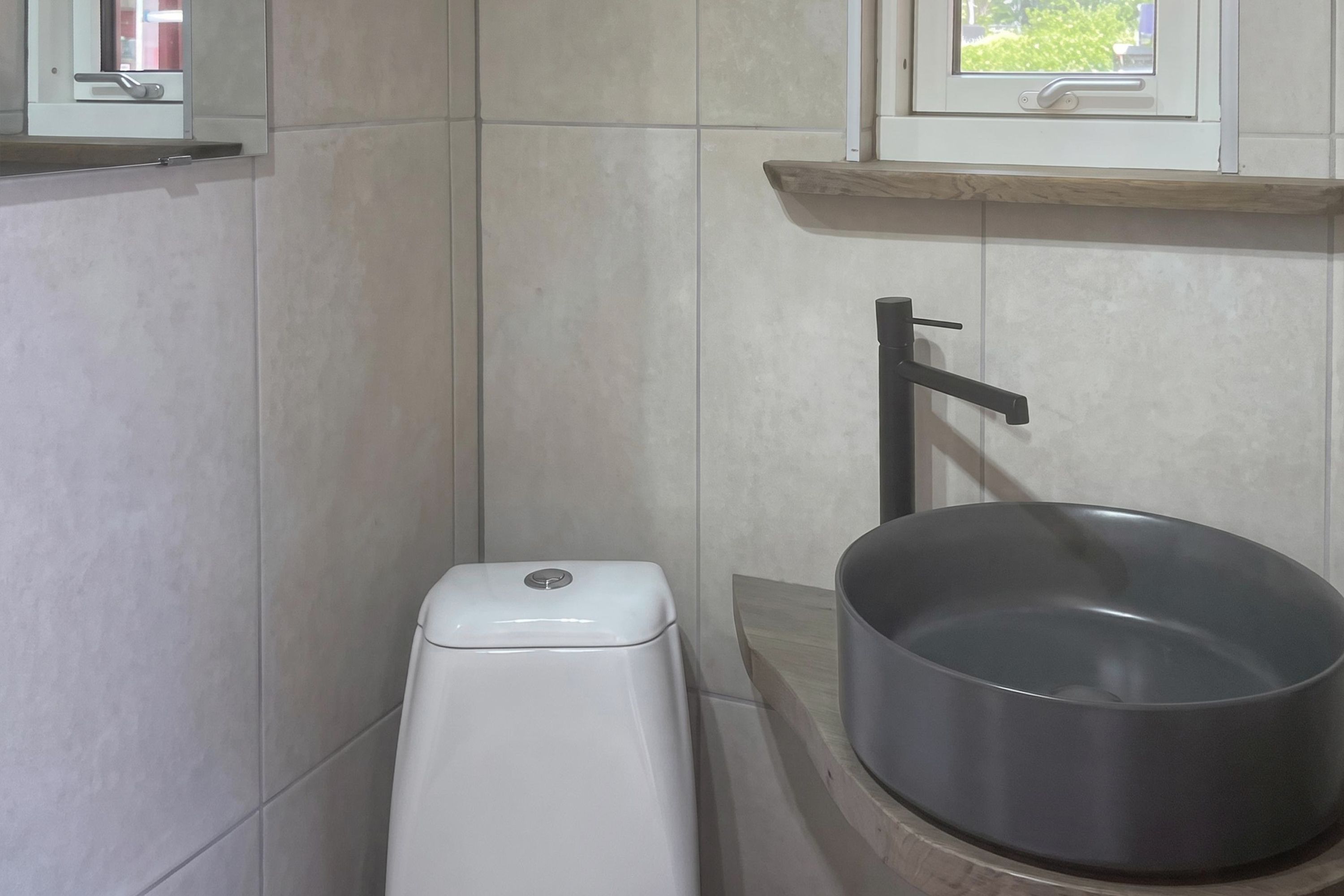 Un baño con inodoro, lavamanos y una ventana sobre el lavamanos.