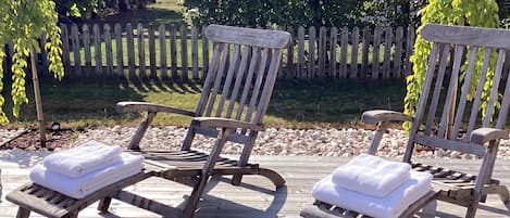 A wooden deck with two lounge chairs, each with a folded white towel.
