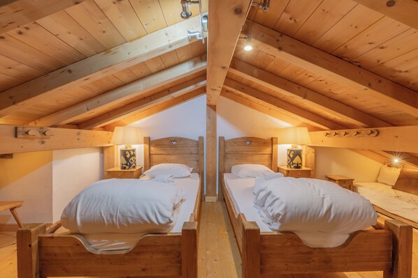 Ein gemütliches Schlafzimmer im Dachgeschoss mit zwei Holzbettgestellen und einem kleinen Tisch dazwischen.