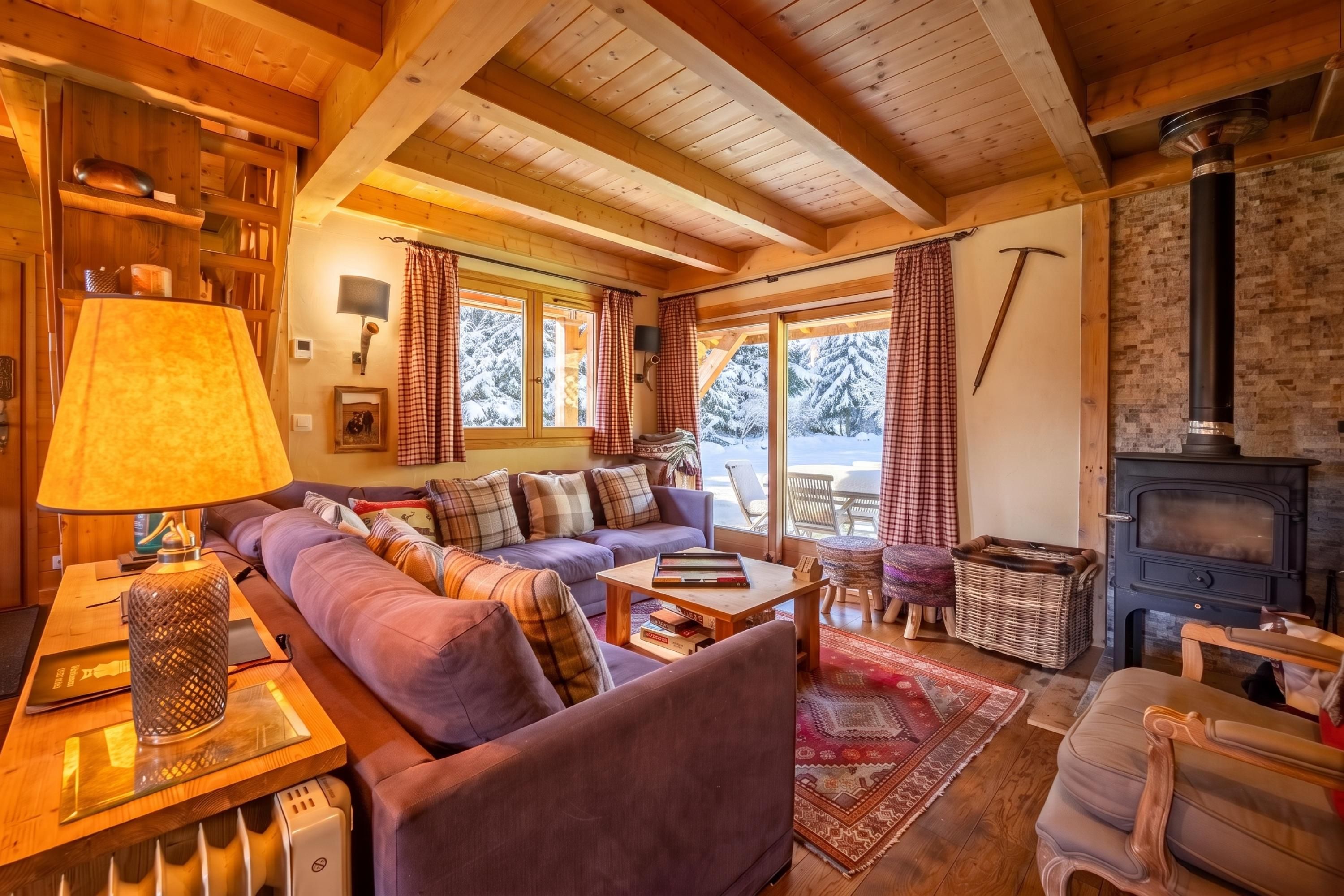A cozy living room with a sofa, a lamp, a fireplace, and a view of snow-covered trees through large windows.