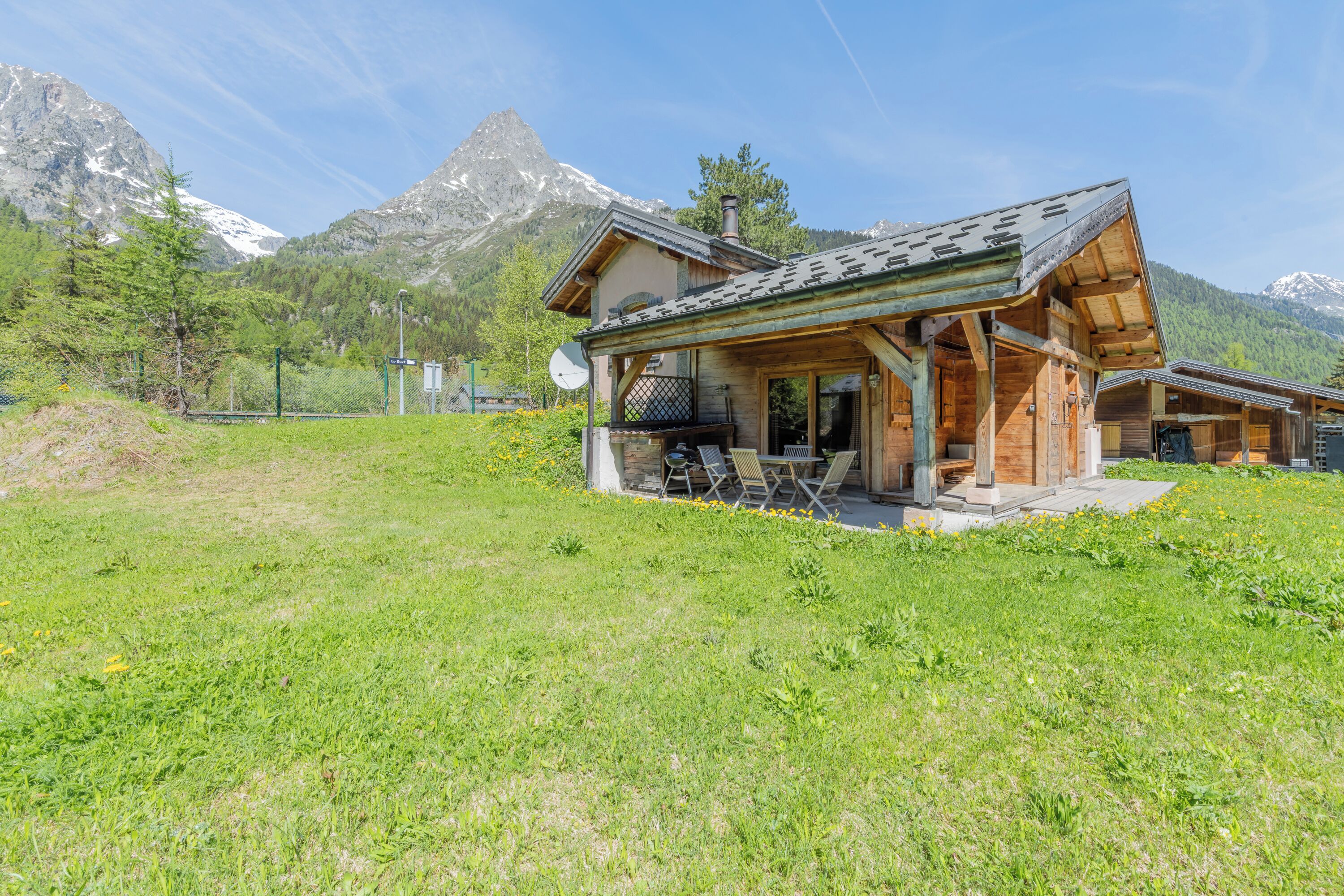Een houten chalet met een schuin dak, een terras met buitenmeubels en een berg op de achtergrond.